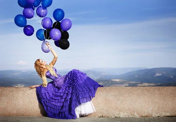 Beautiful woman holding bunch of violet air balloons