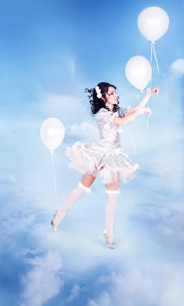 Beautiful girl in a white dress with white balloons flying in the sky