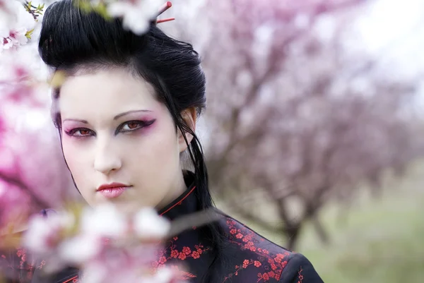 Artistic portrait of japan geisha woman with creative make-up near sakura tree in kimono