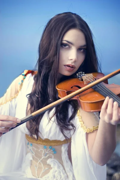 Young attractive woman playing violin on sea background