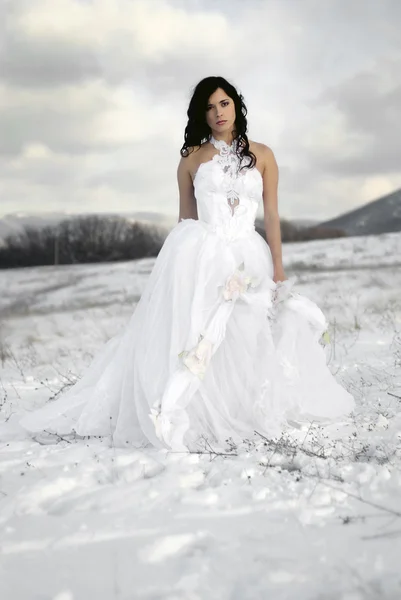 Pretty young woman posing in wedding dress with train, on winter snow