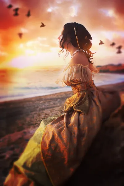 Beautiful girl sits on a cliff at sunset watching the sea