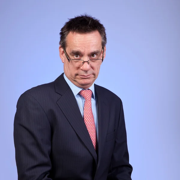 Grumpy Frowning Business Man in Suit Looking over Glasses on Blu