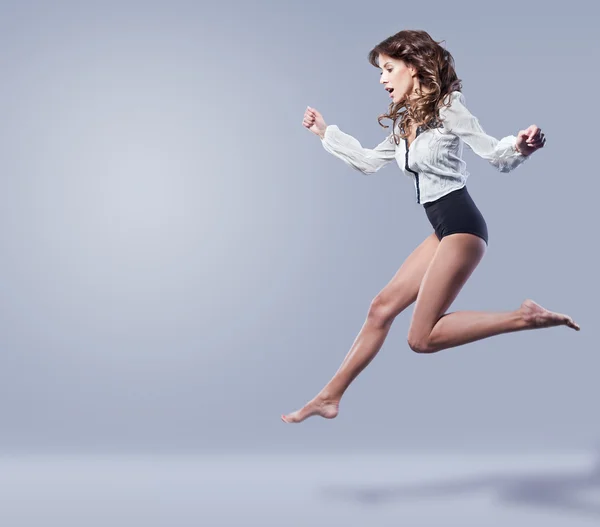 Young beautiful brunette with long legs jumping In Air on a blue background