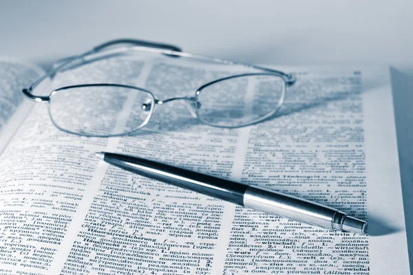 Open dictionary with a pair of glasses and pen
