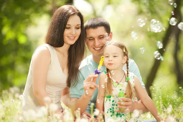 Happy mother, father and daughter blowing bubbles in the park