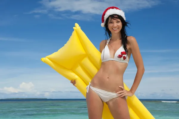Happy santa woman with inflatable mattress on the beach