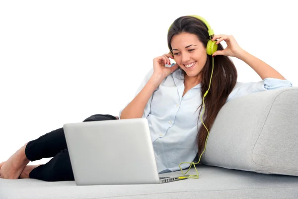 Young woman with earphones and laptop on couch.