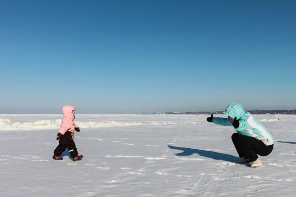 Mother and baby girl walk on snow near the sea