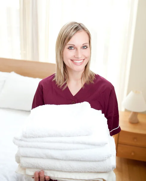 Smiing cleaning lady holding towels in a hotel room