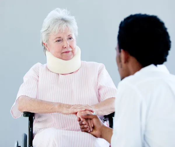 Senior woman sitting on a wheelchair with a neck brace talking w