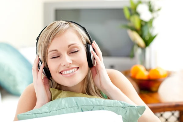 Delighted young woman listening music lying on a sofa