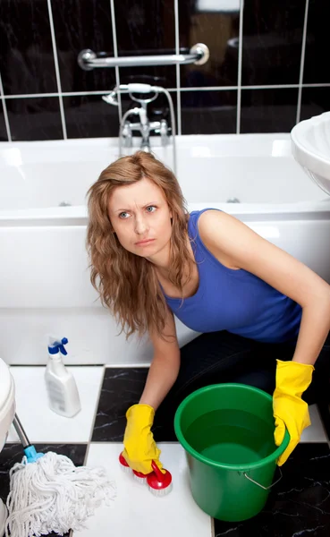 Unhappy woman cleaning bathroom's floor