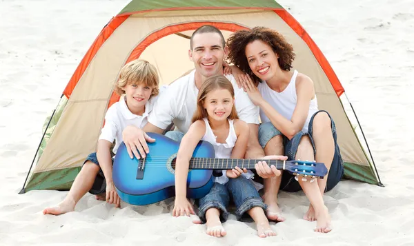 Family camping on beach playing a guitar