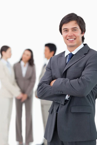 Smiling salesman with arms crossed and team behind him
