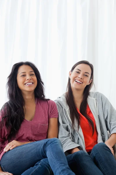 Two laughing women on the couch as they look straight ahead