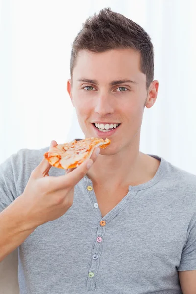 A smiling man holding pizza as he is about to eat