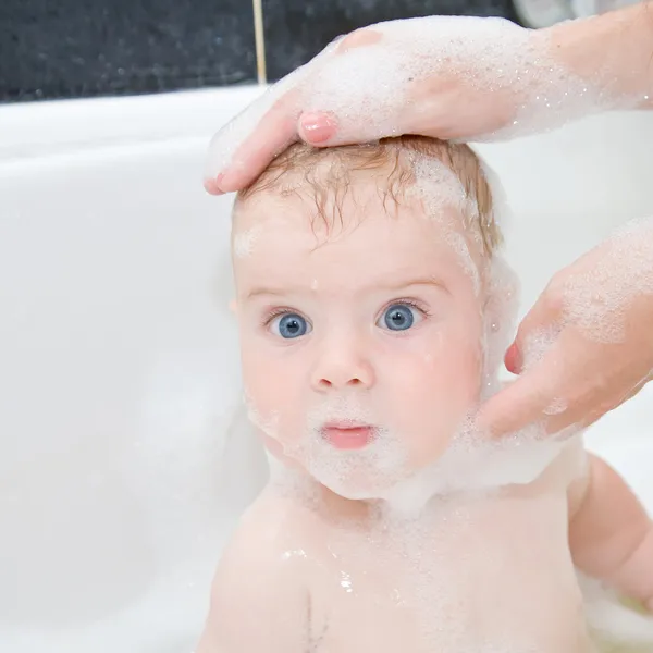 Mother washing baby hair in bath.