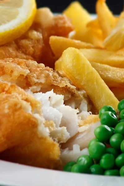 Close up of fish and chips with peas and a slice of lemon.