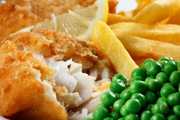 Close up of fish and chips with peas and a slice of lemon.