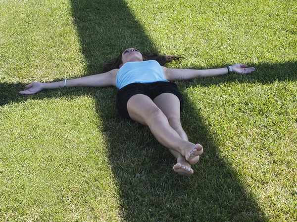 Young woman laying over cross shadow in the grass