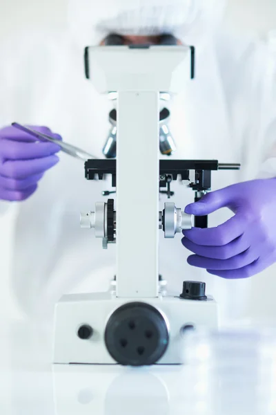 Scientist conducting research in sterile laboratory whilst looking through microscope selective focus