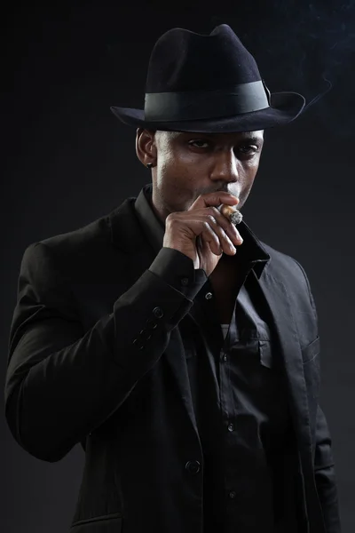 Black man wearing hat and smoking cigar