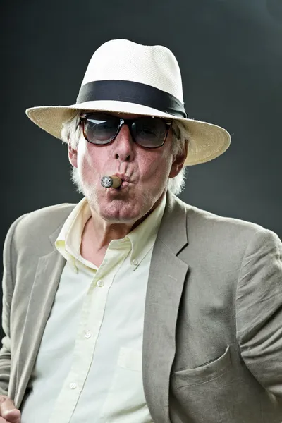 Senior gangster man smoking cigar wearing light suit and hat with vintage sunglasses.