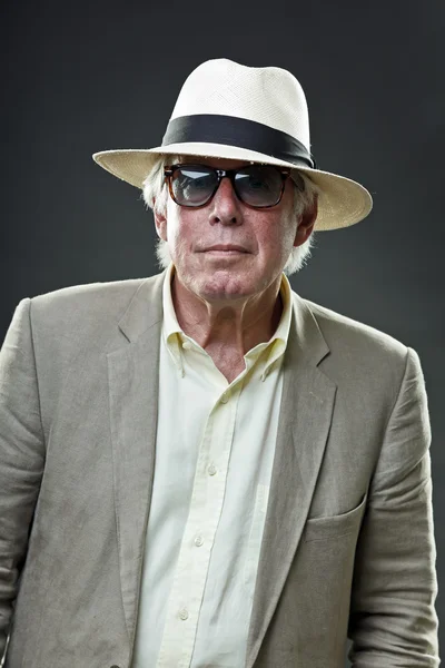 Senior man in suit wearing hat and vintage sunglasses.