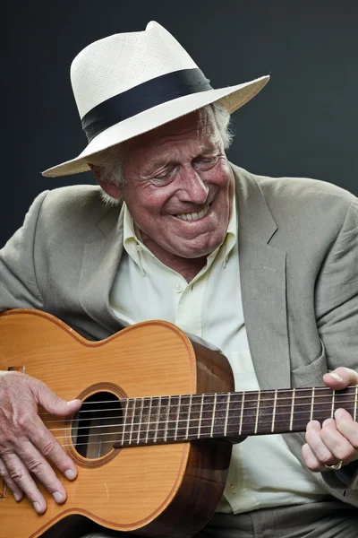 Senior jazz musician playing accoustic guitar. Wearing suit and hat.