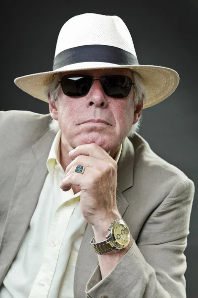 Senior man in suit wearing hat and sunglasses isolated on grey background.