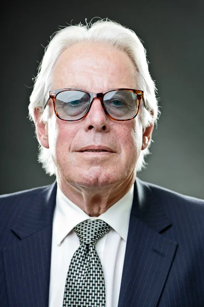 Senior stylish business man wearing vintage sunglasses with dark blue suit and tie.