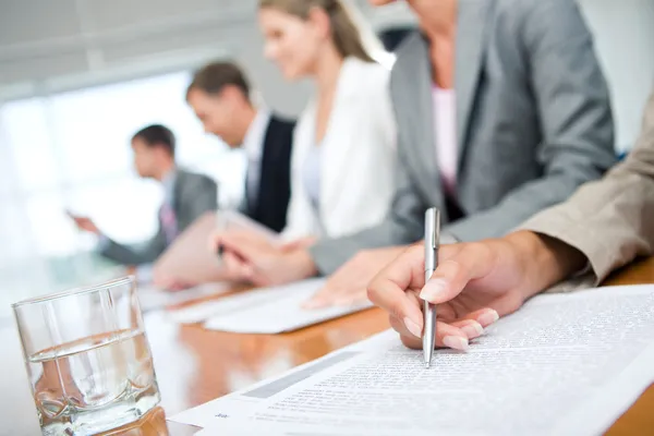 Woman\'s hand with pen over document on background of business group