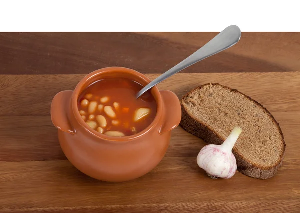 stock image Soup in ceramic pot with bread and garlic on wooden table