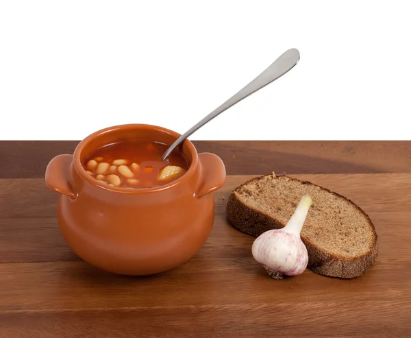 Soup in clay pot with bread and garlic on wooden table — Stock Photo, Image