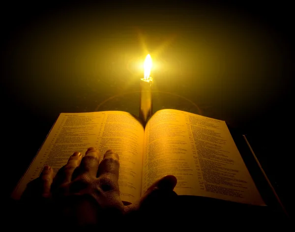在一支蜡烛旁边的桌上打开一本圣经 — 图库照片