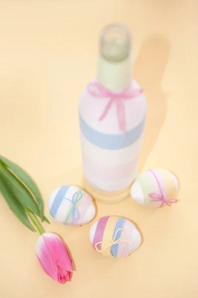 Рожеві тюльпани, великодні яйця та пряжа, загорнута пляшка — стокове фото