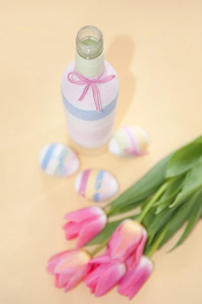 Рожеві тюльпани, великодні яйця та пряжа, загорнута пляшка — стокове фото
