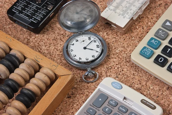 Pocket watch, a calculator, a wooden abacus on a cork board