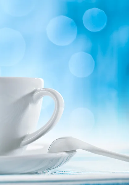 Біла керамічна чашка з ложкою на розмитому синьому фоні — стокове фото