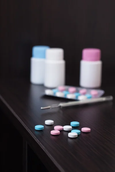 Pillole colorate e termometro sul tavolo marrone — Foto Stock