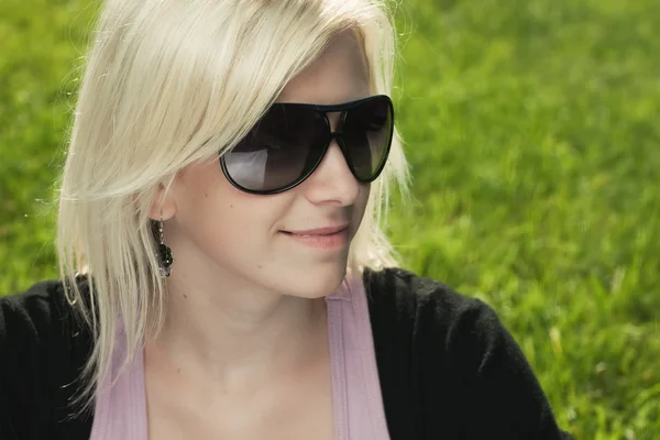 Mladá dívka s sluneční brýle sedí na trávě — Stock fotografie