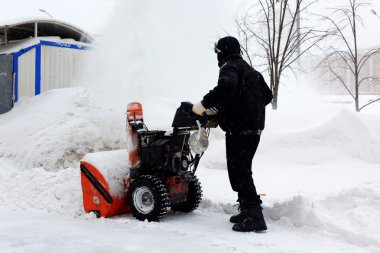 Snowblower in city under snowfall clipart