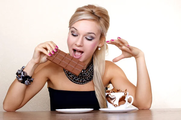 Woman with cup and chocolate against yellow wall at table — Stock Photo, Image