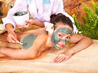 Young woman having clay body mask. clipart