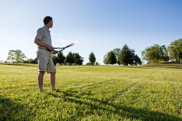 Старший человек стрижет траву ножницами — стоковое фото