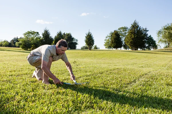 Homem sênior cortando grama com tesouras — Fotografia de Stock