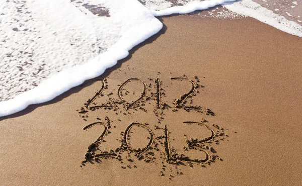 2012 y 2013 escrito en arena con olas — Foto de Stock