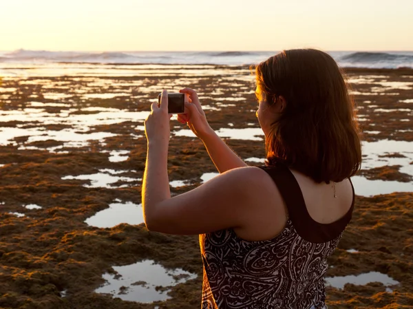 Foto's nemen meisje voor zonsondergang op telefoon — Stockfoto
