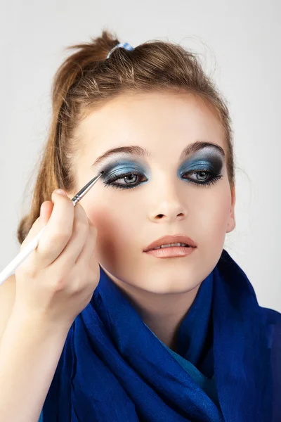 Proceso de hacer maquillaje. Maquillaje artista que trabaja con cepillo en la cara del modelo. Retrato de mujer rubia joven en el interior del salón de belleza . — Foto de Stock